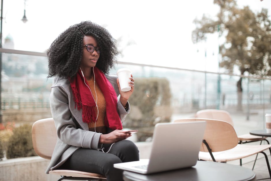 Confident woman working remotely in an outdoor café, sipping coffee and using a laptop.