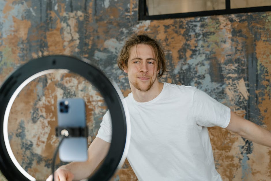Man filming vlog with smartphone and ring light in an indoor setting. Casual attire.