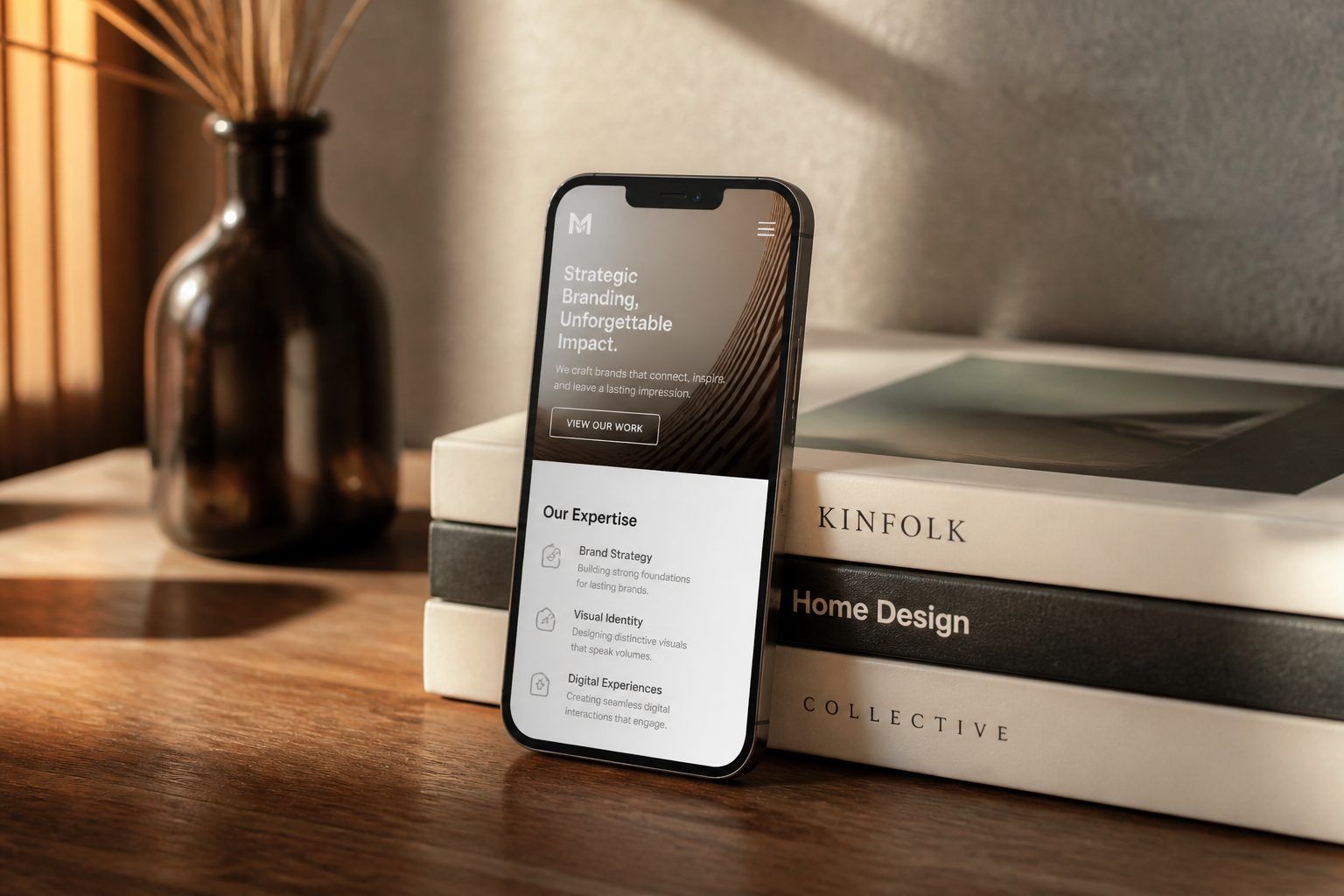 a smartphone displaying a clean, modern business website homepage propped against a stack of design books on a wooden surface, warm side lighting, no people, product-style photography
